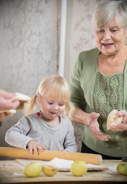 An old woman making little pies with her granddaughter exited girl rolling the dough