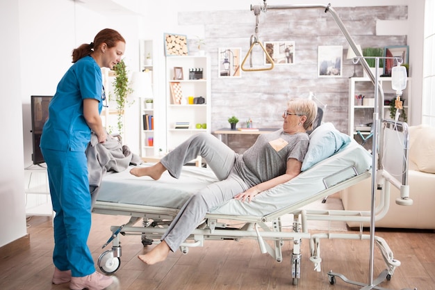 Old woman in nursing home laying on bed with help from health visitor.