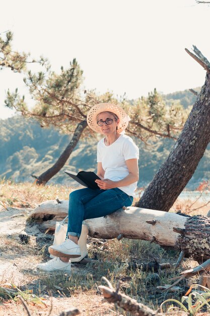 Old woman reading a book at the beach during a super sunny day. Freedom concept with copy space, relaxation and senior retirement happiness, Smiling to camera