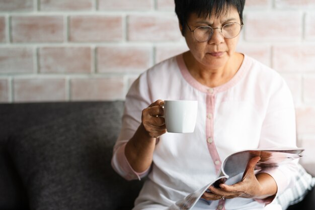 歳の女性が自宅で一杯のコーヒーで本を読んで