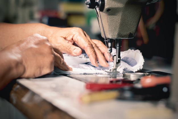 The old woman's hand is using a sewing machine.