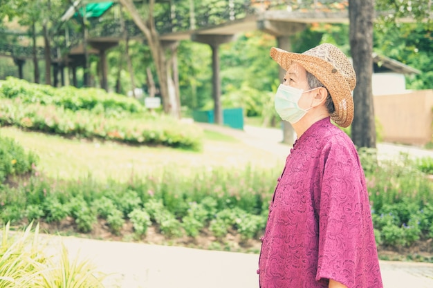 Old woman wearing medical mask resting in garden