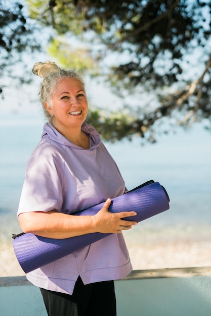 Old woman with dreadlocks walking with her mat to yoga or pilates class in park copy space well being and leisure activity concept