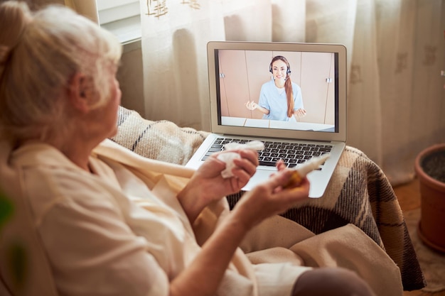 Old woman with flu having online consultation with doctor at home