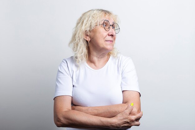 Old woman with glasses looks to the side on a light background.