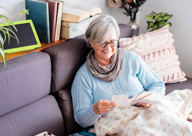 old woman with gray hair remembers the past looking at old photographs of a lifetime sitting on sofa