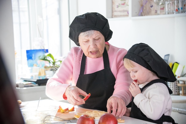 An old woman with a little girl in the kitchen a little girl eats a piece of apple