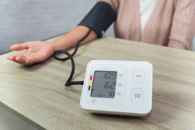 Old woman with pressure gauge checking blood pressure level on the table