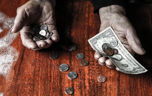 Old woman with very little money. Poverty concept. Pensioner with one dollar note and coins in hands. Economy and crisis in the world.