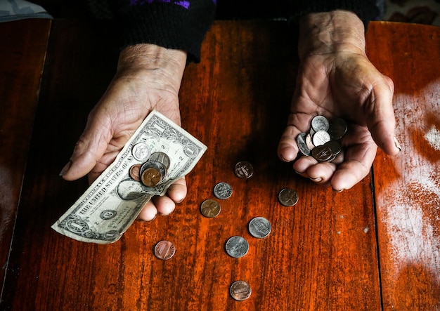 Old woman with very little money. Poverty concept. Pensioner with one dollar note and coins in hands. Economy and crisis in the world.