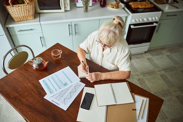 Old woman writing on spiral notebook at home