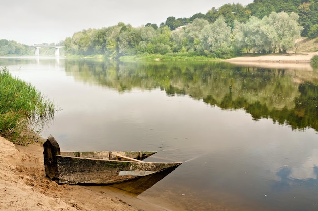 An old wooden boat half submerged in the water on a misty summer morning overlooking the bridge