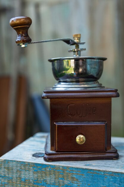 An old wooden coffee grinder on a blue bench. Close-up. Vertical.