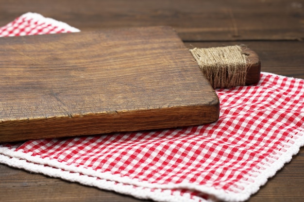 Vecchio tagliere di legno e tovagliolo da cucina di cotone rosso e bianco piegato su uno sfondo marrone di legno, vista dall'alto, spazio di copia