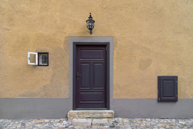 Old wooden door on rustic old world style concrete yellow wall with small window on the side