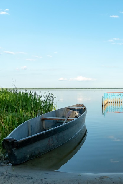 An old wooden fishing boat docked on a deserted sandy beach View of a quiet and calm lake without ripples on the water Reflection in the clear water of the blue sky and fluffy clouds during sunset