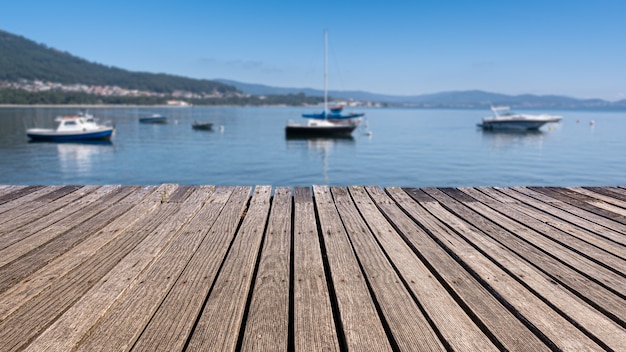 Foto vecchia passerella in legno in riva al mare con sfondo sfocato e barche