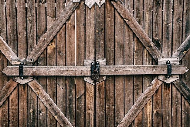 Old wooden gate with hanging big black iron barn lock,\
selective focus