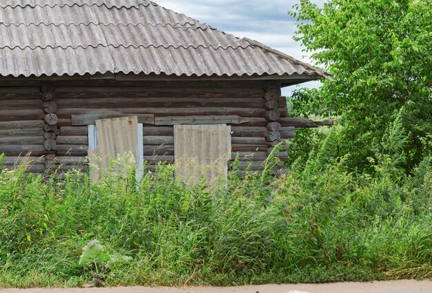 Old wooden house overgrown with tall grass. Abandoned country house. Rural scene.