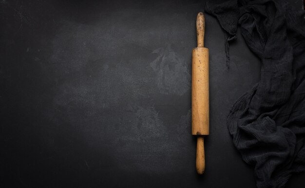 Old wooden rolling pin for rolling dough on a black background top view Copy space