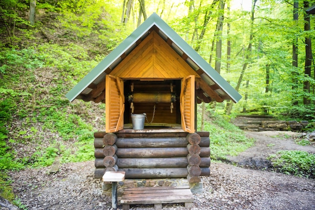 Old wooden well with metal bucket in green forest