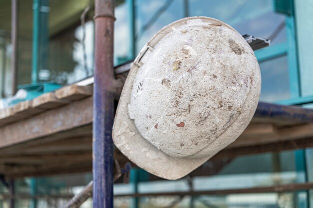 An old work helmet hangs on the scaffolding. Blurred background. Builder hard work concept.