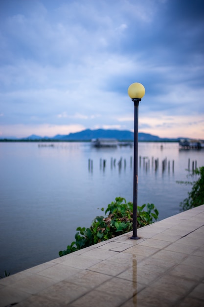 Old Yellow street light post on the walkway near the lake with blurred view.