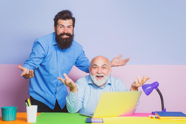 Old and young men looking at laptop screen watching movie or news in social network smiling broker c