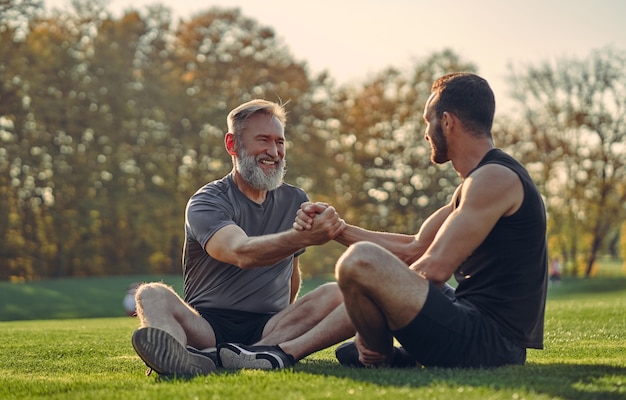 The old and young sportsmen handshaking on the grass