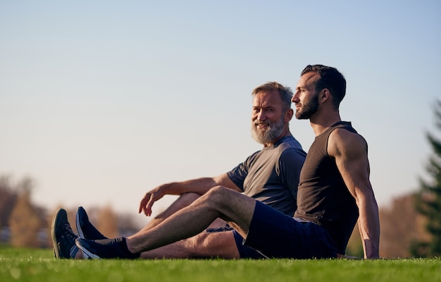 The old and young sportsmen sitting on the grass