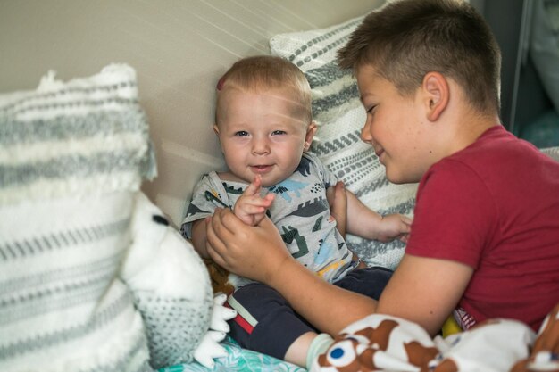 Photo older brother hugs baby cute boy and his brother relaxing in a white bedroom family with children at home love trust and tenderness