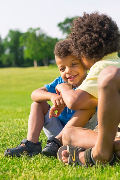 The older brother is telling a secret to the younger one on a sunny glade