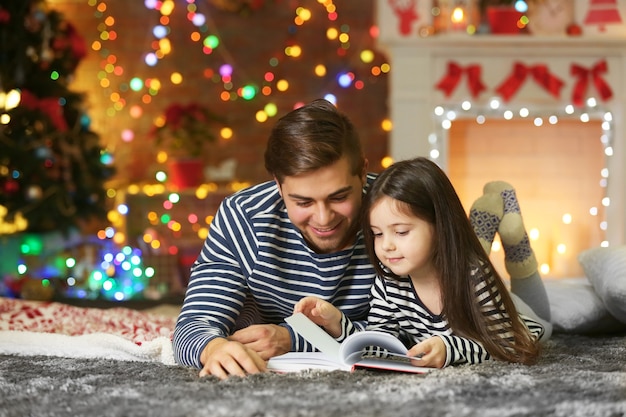 Старший брат с младшей сестрой читают книгу в рождественской гостиной