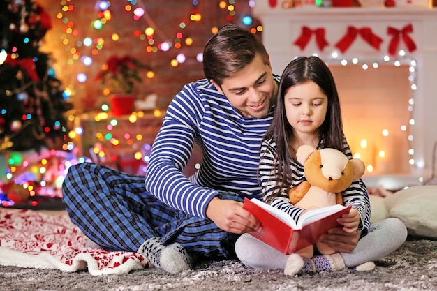Старший брат с младшей сестрой читают сказку в рождественской гостиной