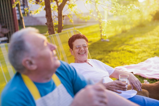 older happy couple resting in chair in their backyard