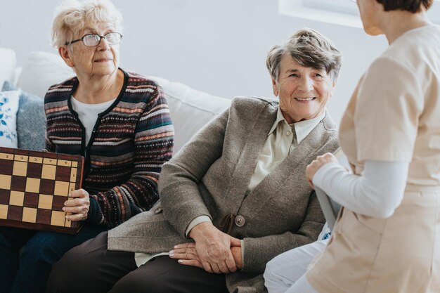 Photo older ladies sit on a couch and talk to a nurse at a local nursing home