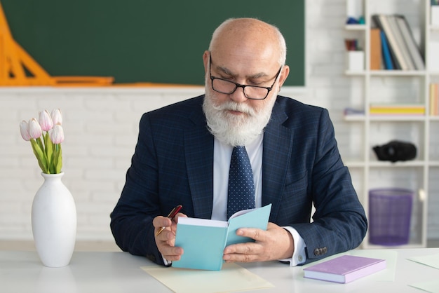 Older male teacher standing in front of a chalkboard in a classroom