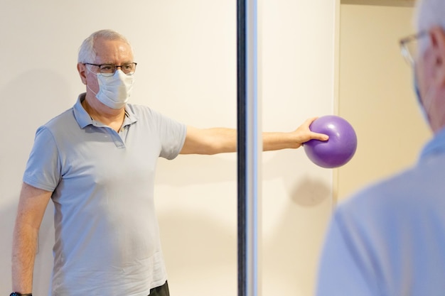 Older man doing kinesiology exercises to recover from shoulder\
tendinitis with a medicine ball