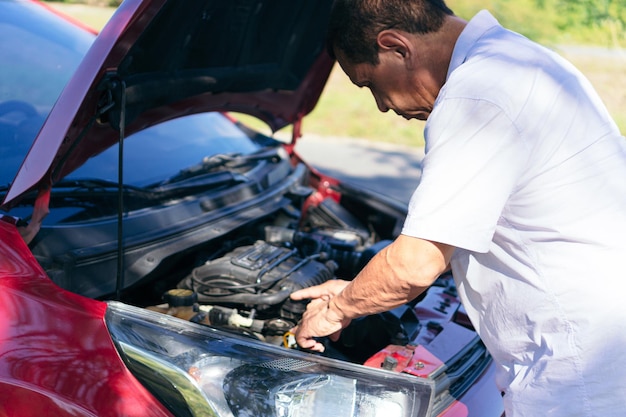 Older man repairing his car on road.