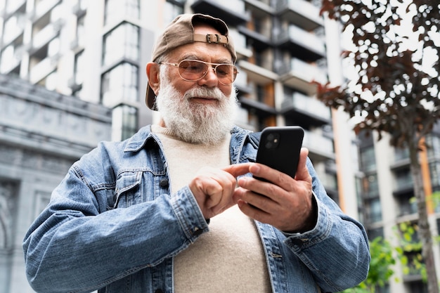 Foto uomo anziano che utilizza smartphone all'aperto in città