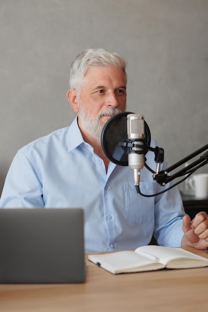 Older man with gray hair irecording podcast in recording studio with microphone and headphones