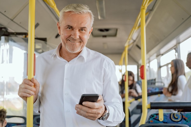Пожилой мужчина с седыми волосами в рубашке едет на автобусе с улыбкой