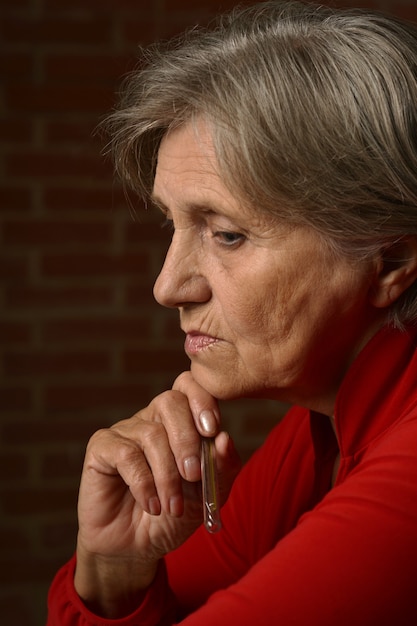 Older sick woman in red with thermometer on a background