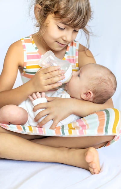 An older sister is feeding a newborn baby