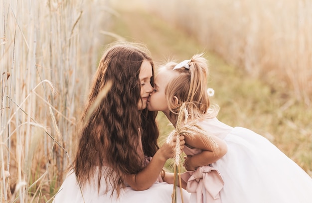 Older sister kisses the cheek of the younger in the summer in nature. Kids hug.