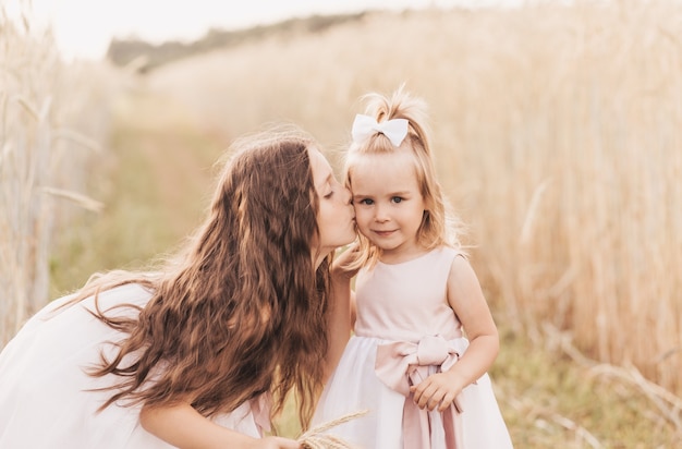 Older sister kisses the cheek of the younger in the summer in nature. Kids hug.