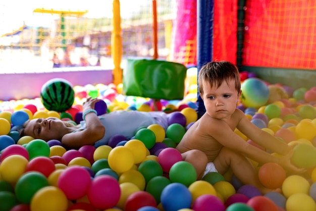 The older sister plays with her younger brother and throws\
small balls at him while sitting in the playroom