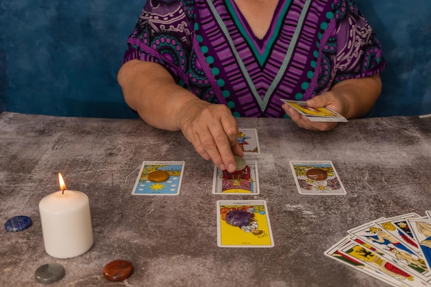 older white-haired woman reading tarot cards on a wooden table with candle