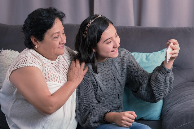 Older woman 60 year old latin grandmother using cell phone and having fun with her granddaughter taking photos and watching videos