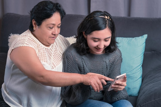 Older woman 60 year old latin grandmother using cell phone and having fun with her granddaughter